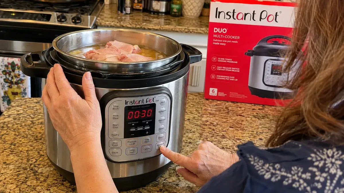 A hand pressing a button on the Instant Pot Duo control panel after adding a raw chicken breast and broth to the inner pot.
