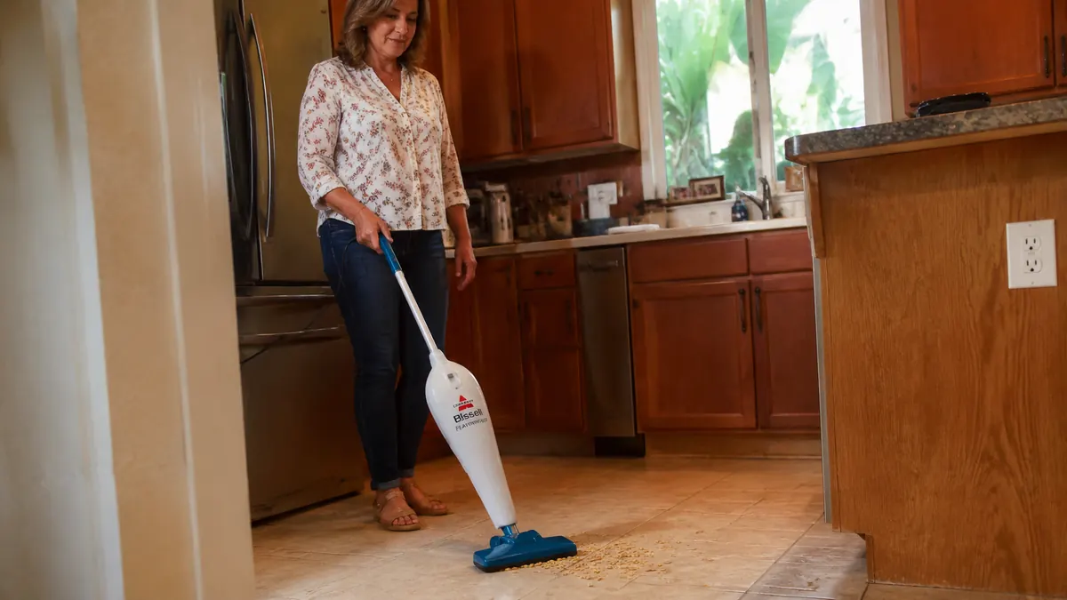 Woman's hand running the Bissell Featherweight over spilled cereal on a kitchen tile floor