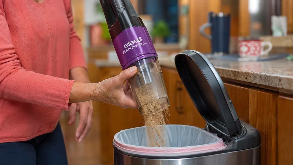 Close-up of the Bissell Featherweight's dust cup being emptied over a kitchen trash can