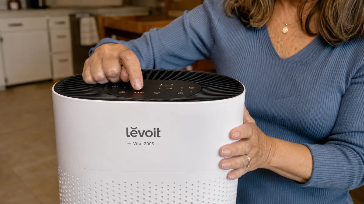 A hand adjusting the auto mode button on the control panel of a white cylindrical air purifier