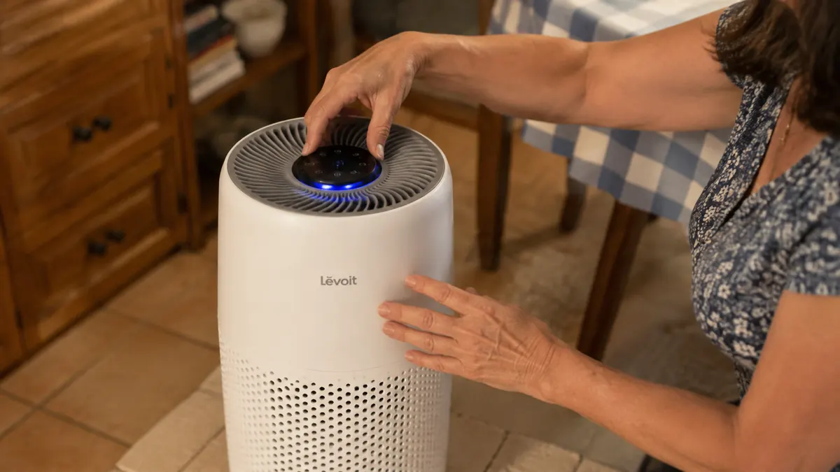 Hand adjusting the top control ring on the Levoit Vital 200S air purifier while it runs on a dresser