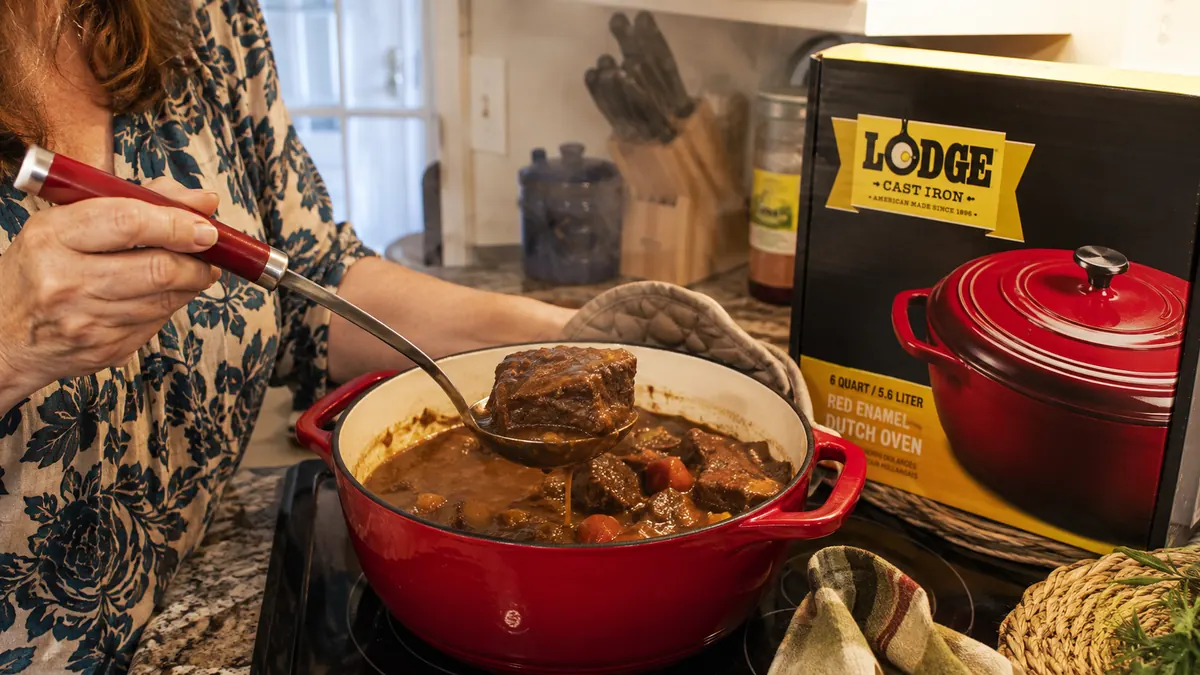 Hands ladling braised short ribs out of a Lodge Dutch oven on the stovetop