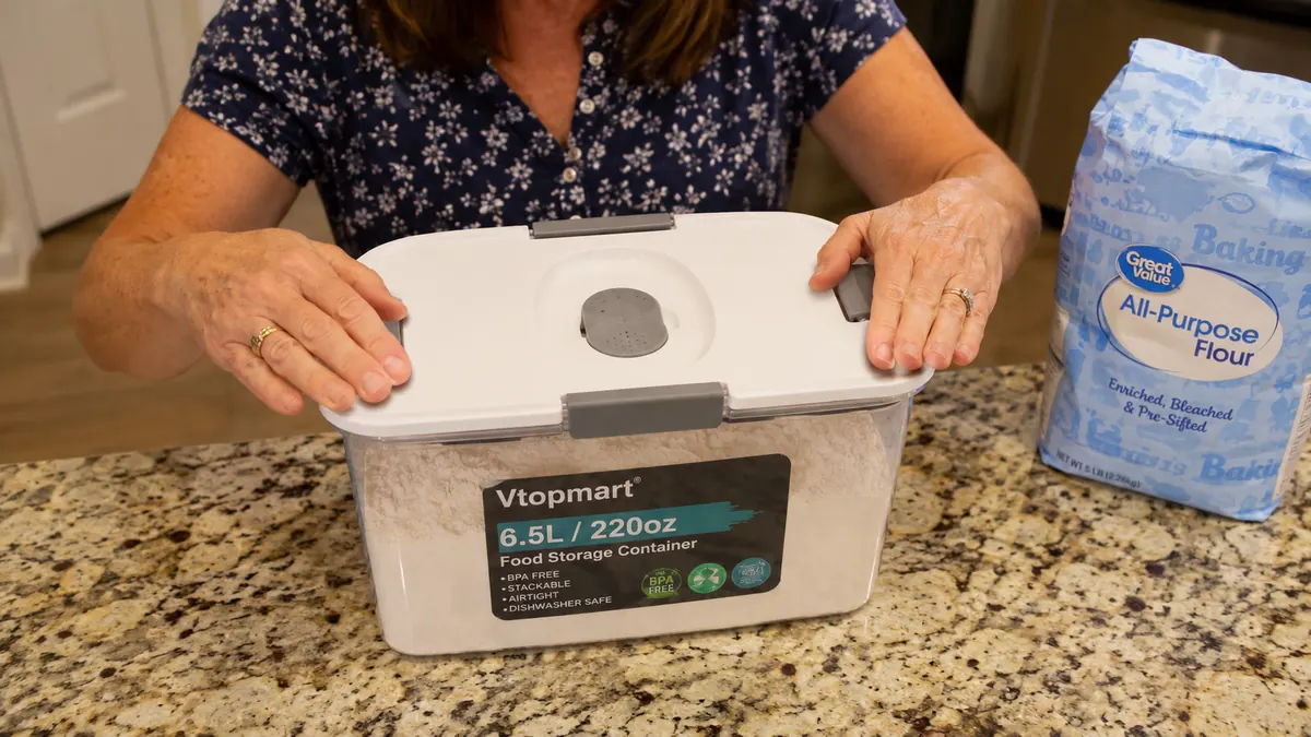 Hands pressing down the button seal on a Vtopmart container lid over a bin of flour